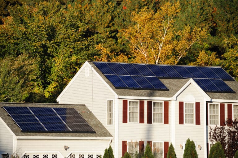 Beautiful white New England home with red shutters. Newly installed solar panels on the roof and a lush forest in the backyard.
