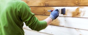 worker painting house exterior with brown wood protective color