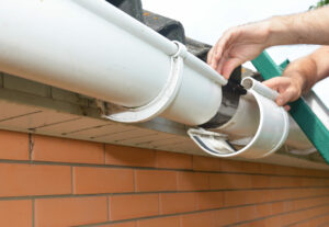 Attaching sections of a white half-round gutter system to a house.