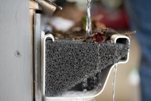 Water flows over a foam gutter guard, covered with leaves and debris, highlighting effective rainwater filtration.