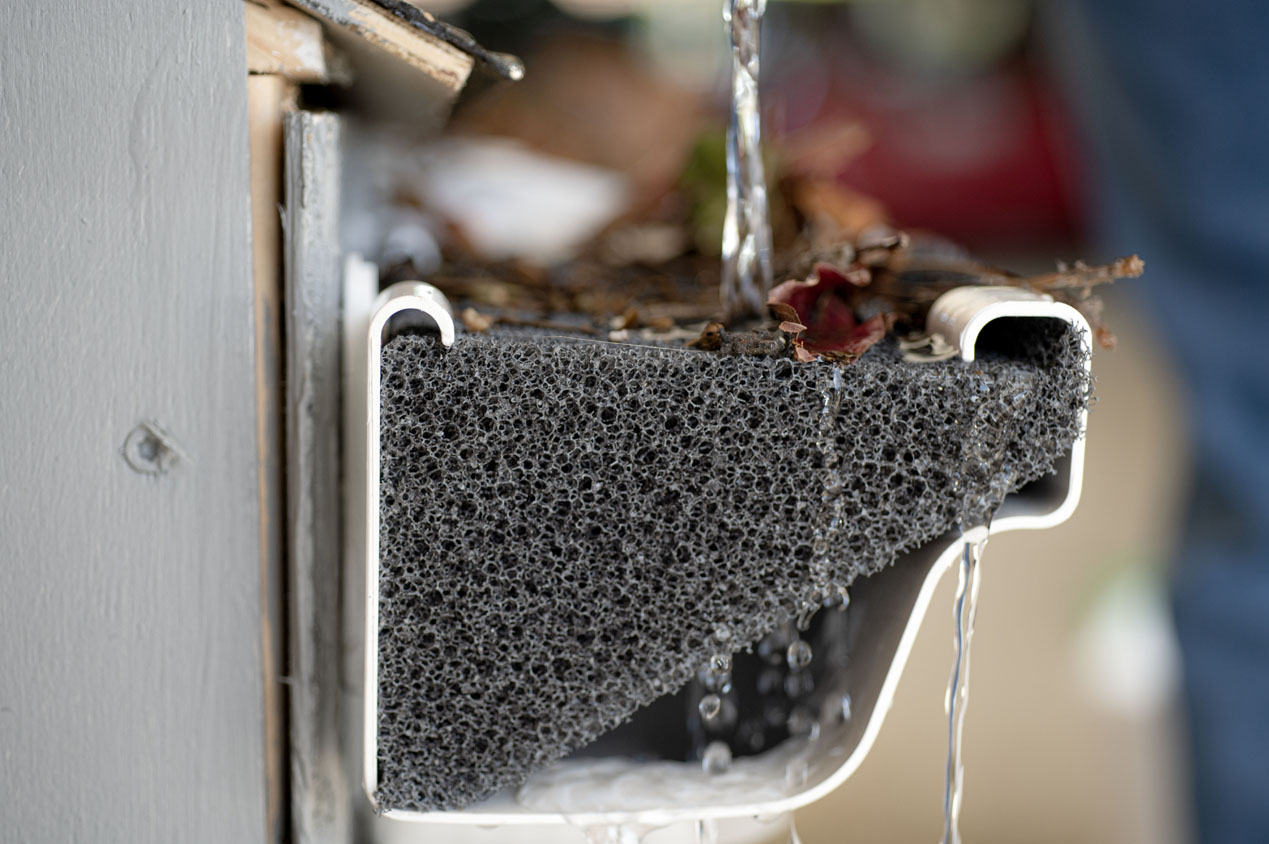 Water flows over a foam gutter guard, covered with leaves and debris, highlighting effective rainwater filtration.