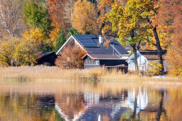 An image of a house at the lake with solar panels on the roof